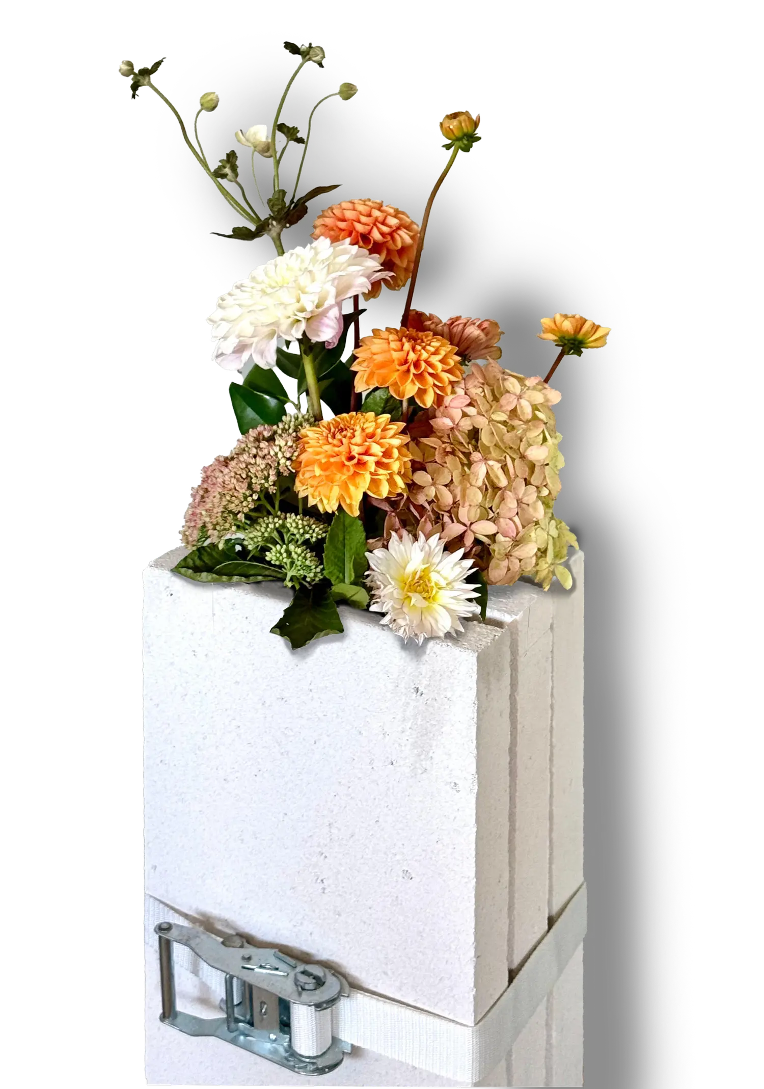Composizione floreale con dalie e ortensie su una colonna di blocchi in cemento cellulare, legata con una cinghia a cricchetto